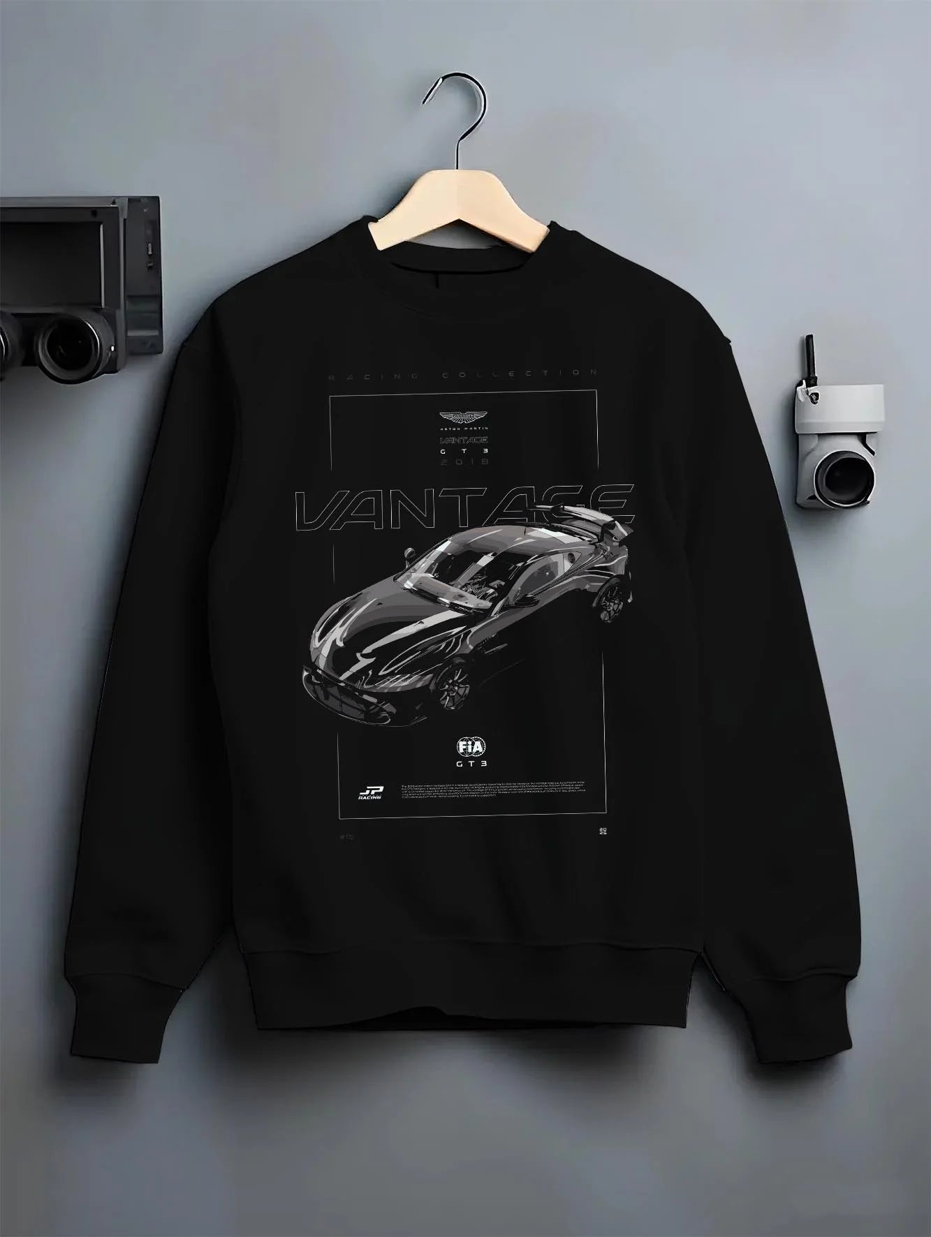 Black crewneck sweatshirt on a hanger against a grey wall, featuring Aston Martin Vantage gt3 rs racing motorsport street graphic.