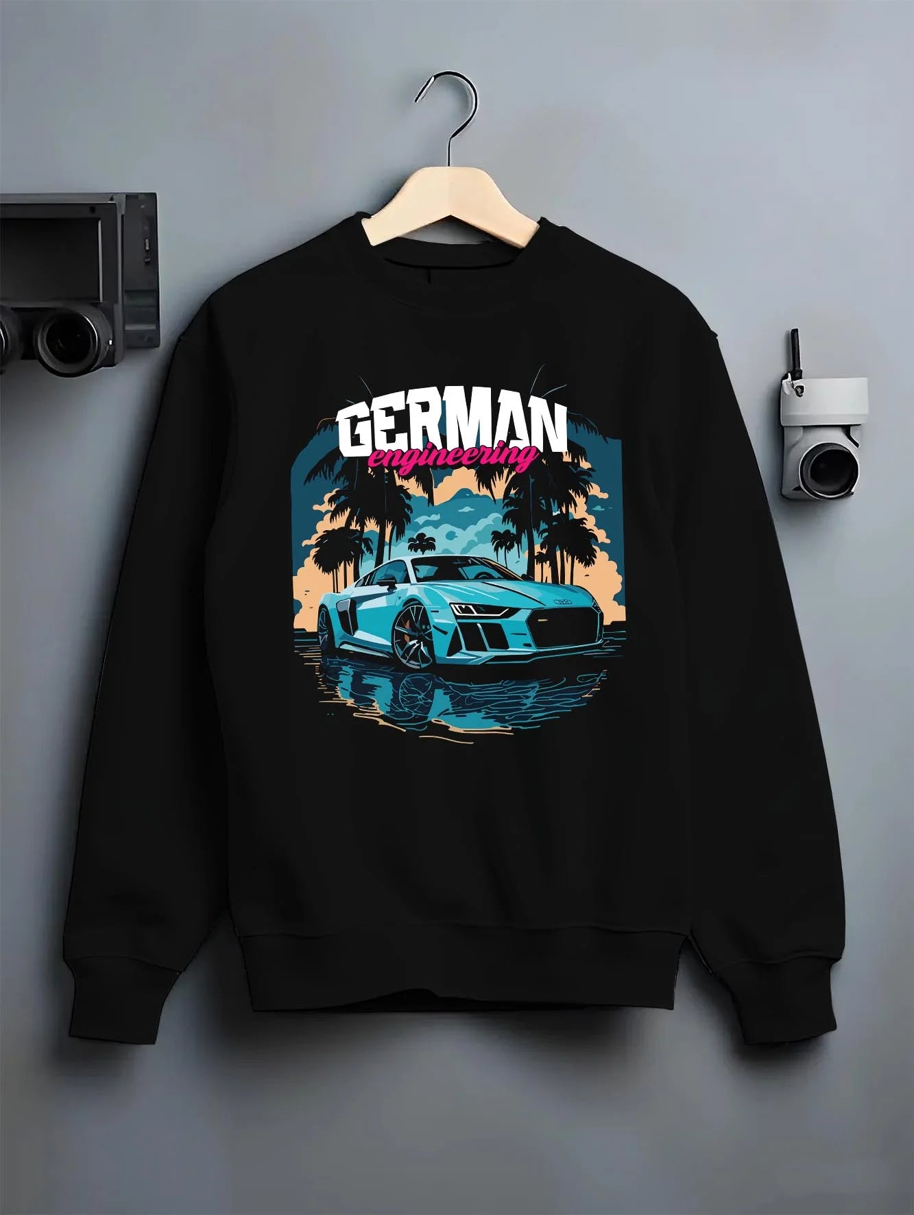 Black crewneck sweatshirt on a hanger against a grey wall, featuring Audi R8 german street racing performance motorsport graphic.