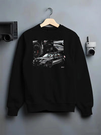 Black crewneck sweatshirt on a hanger against a grey wall, featuring BMW M3 rs motorsport german racing street performance graphic.