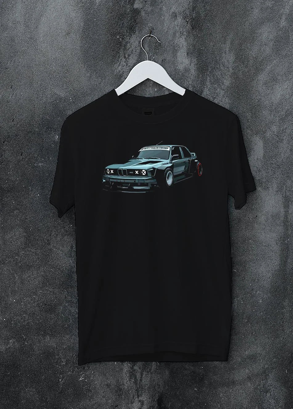Black crewneck T-shirt on a hanger against a grey wall, featuring BMW E30 rs drift jdm stance widebody racing graphic.