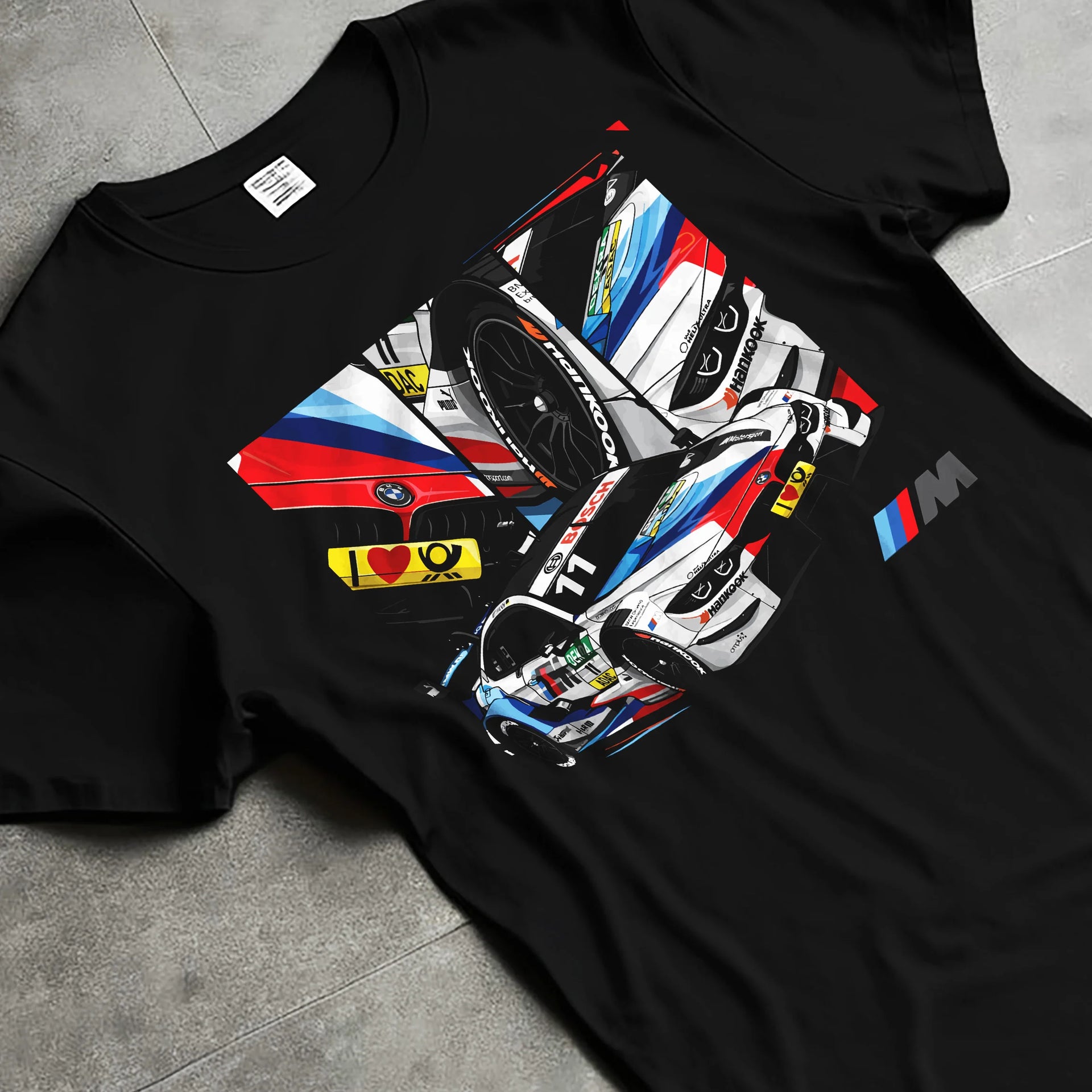 Black T-shirt laid flat with natural fabric folds, featuring BMW M4 rs racing motorsport street performance automotive graphic.