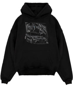 Black pullover hoodie laid flat on a white background, featuring BMW M4 german tuner street racing performance motorsport graphic.