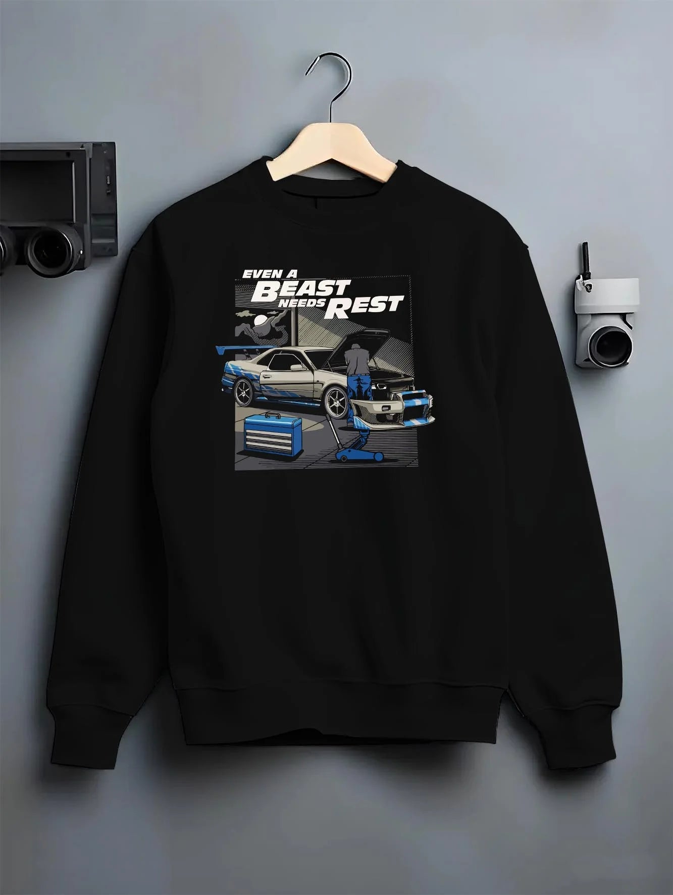 Black crewneck sweatshirt on a hanger against a grey wall, featuring racing tuner street retro beast performance motorsport graphic.