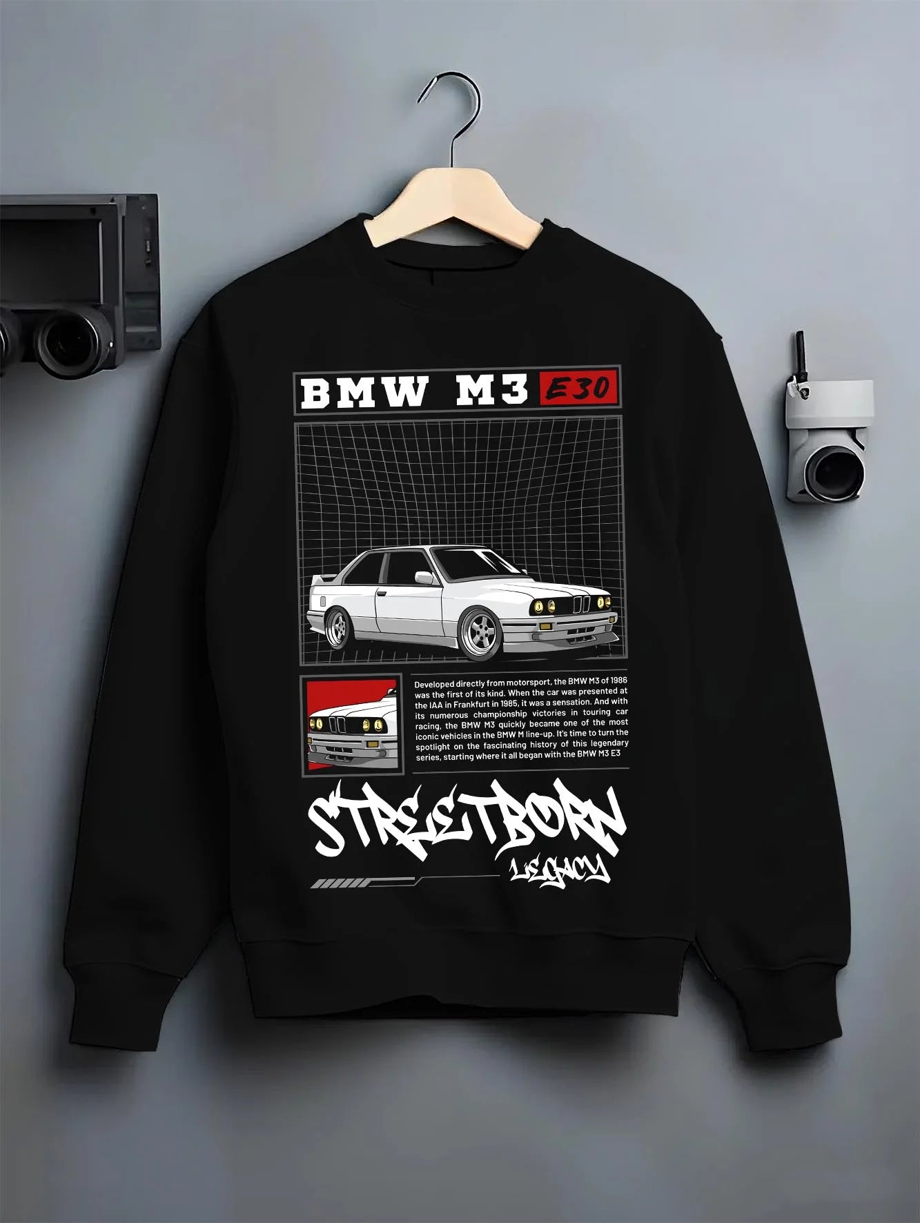 Black crewneck sweatshirt on a hanger against a grey wall, featuring BMW rs turbo racing drift motorsport euro street retro graphic.