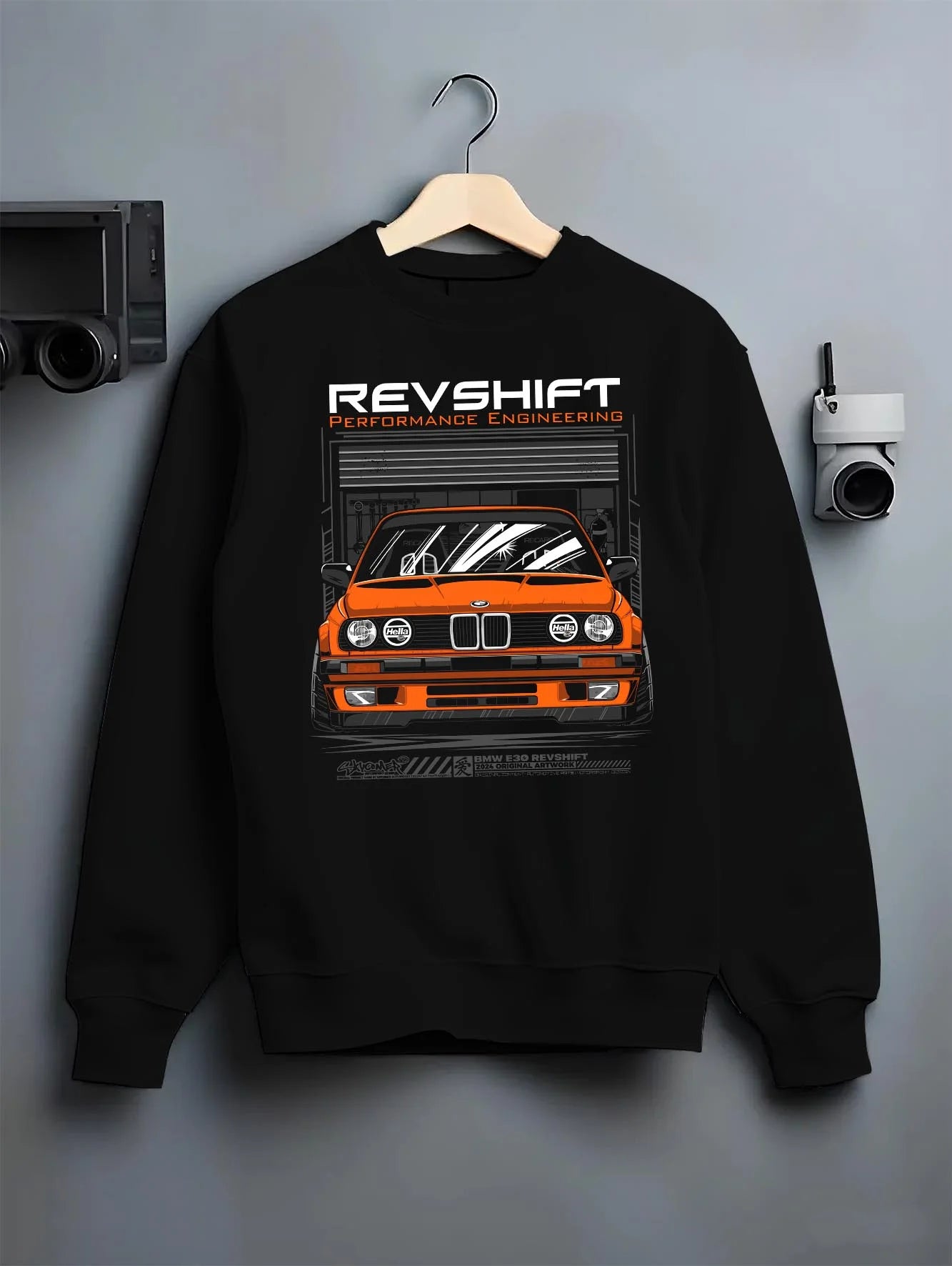 Black crewneck sweatshirt on a hanger against a grey wall, featuring BMW E30 rs motorsport street vintage classic racing graphic.