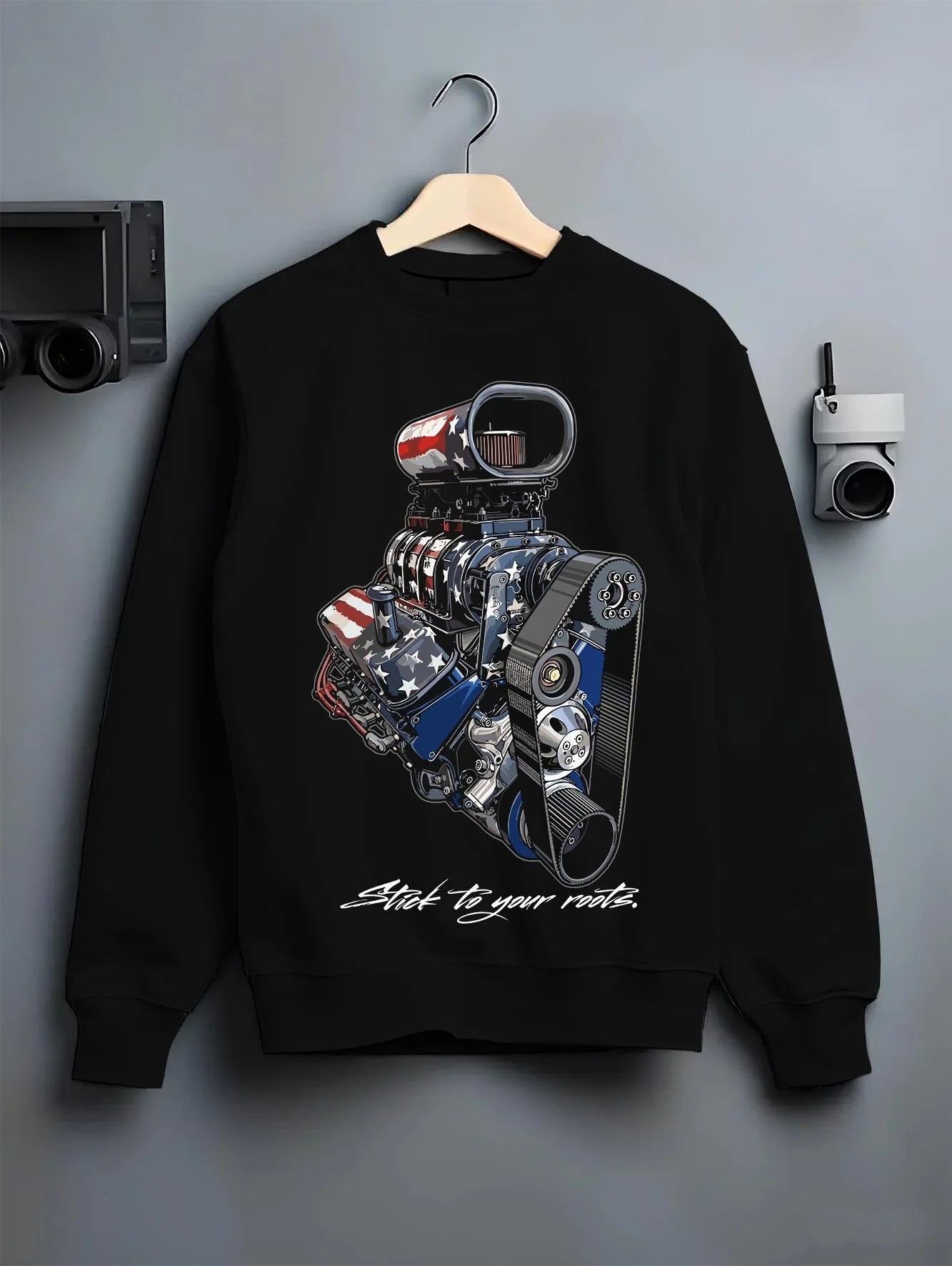 Black crewneck sweatshirt on a hanger against a grey wall, featuring v8 american muscle retro classic enthusiast racing graphic.