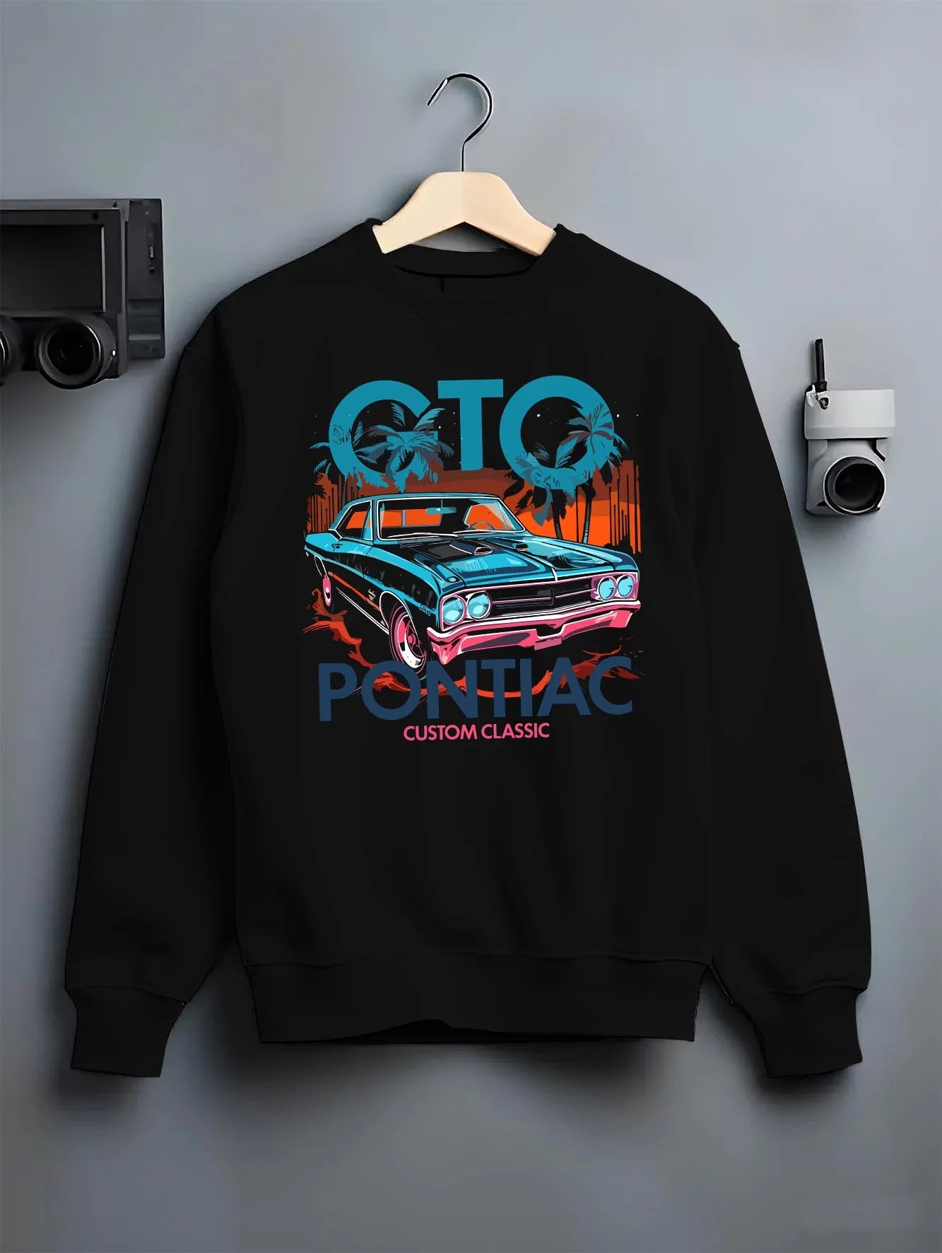 Black crewneck sweatshirt on a hanger against a grey wall, featuring Pontiac GTO muscle street retro vintage classic graphic.