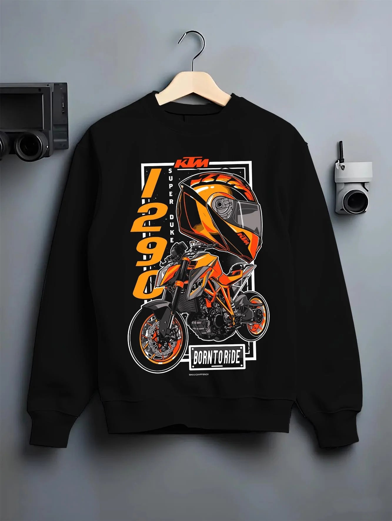 Black crewneck sweatshirt on a hanger against a grey wall, featuring KTM racing street performance motorsport automotive graphic.