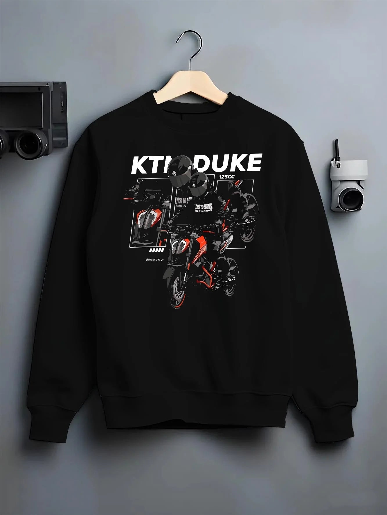 Black crewneck sweatshirt on a hanger against a grey wall, featuring KTM rs racing street performance motorsport automotive graphic.