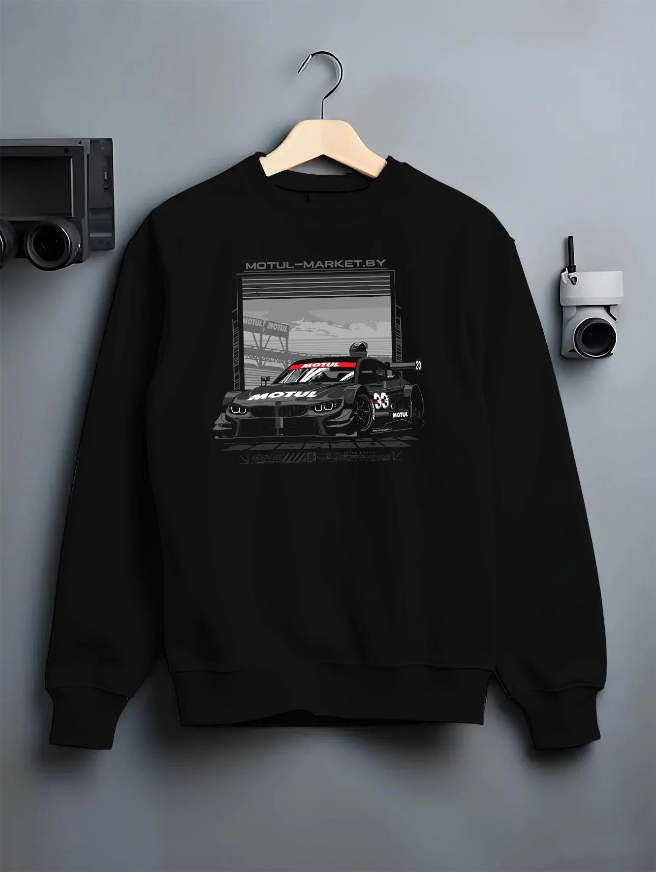 Black crewneck sweatshirt on a hanger against a grey wall, featuring BMW M4 rs turbo racing motorsport german street graphic.