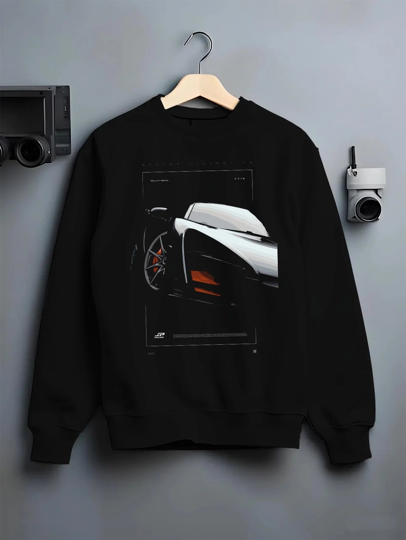 Black crewneck sweatshirt on a hanger against a grey wall, featuring McLaren F1 rs racing street retro speed enthusiast graphic.