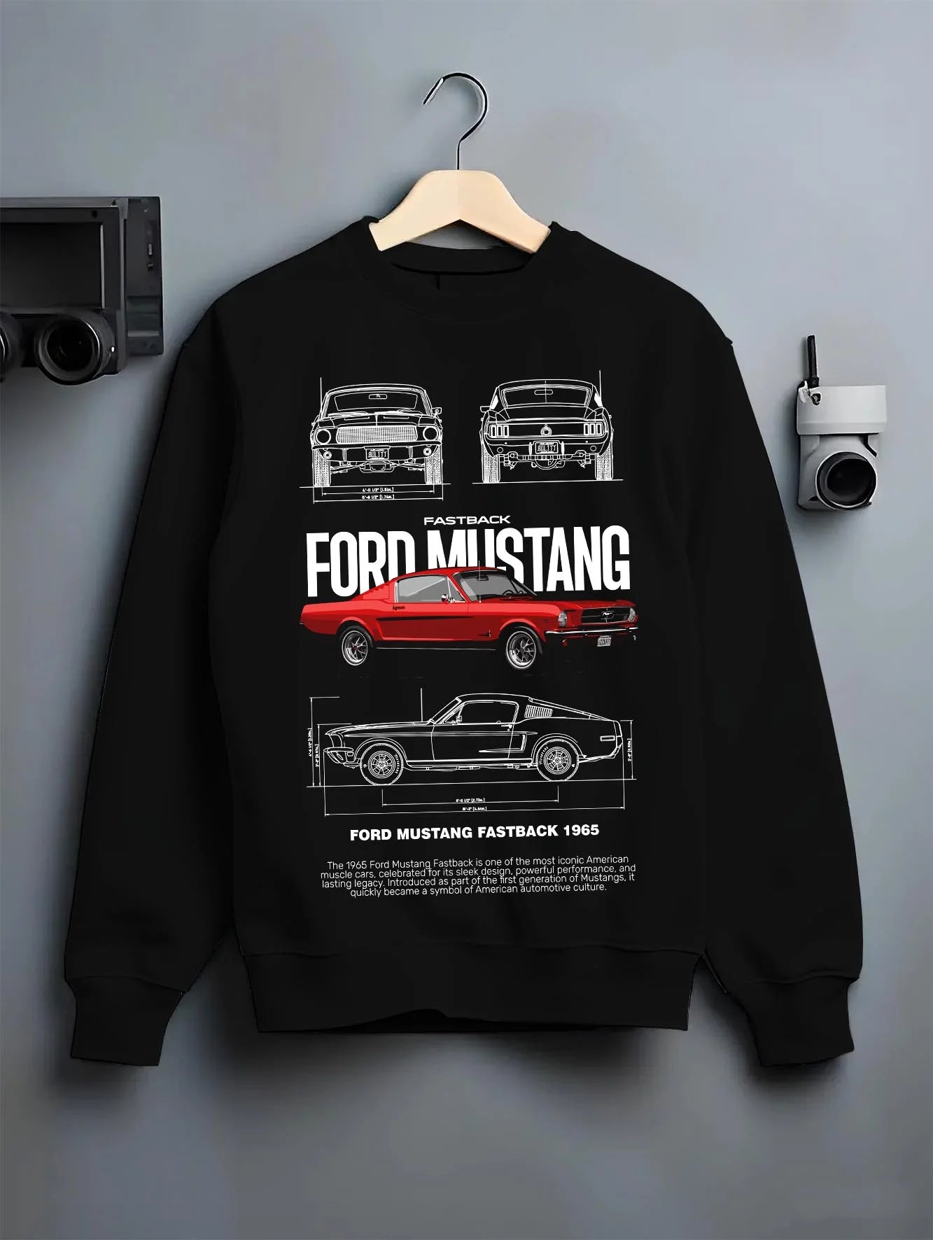 Black crewneck sweatshirt on a hanger against a grey wall, featuring Ford Mustang american muscle retro classic enthusiast graphic.