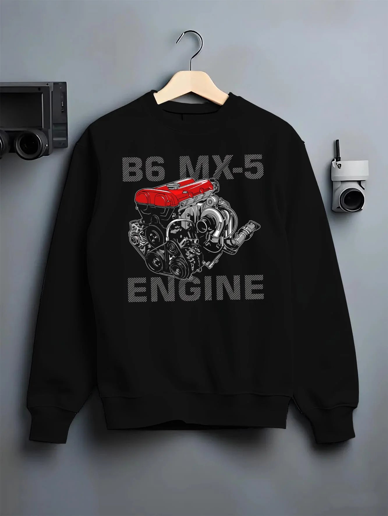 Black crewneck sweatshirt on a hanger against a grey wall, featuring Mazda MX-5 jdm tuner street racing performance graphic.