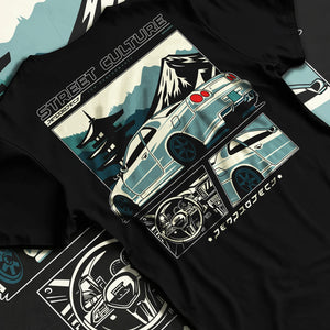 Black T-shirt laid flat with natural fabric folds, featuring Nissan Skyline drift jdm japanese tuner street retro graphic.