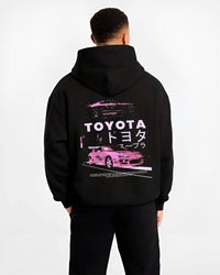 Black hoodie worn by a male model, back view, featuring Toyota Supra racing drift jdm japanese tuner street retro graphic.