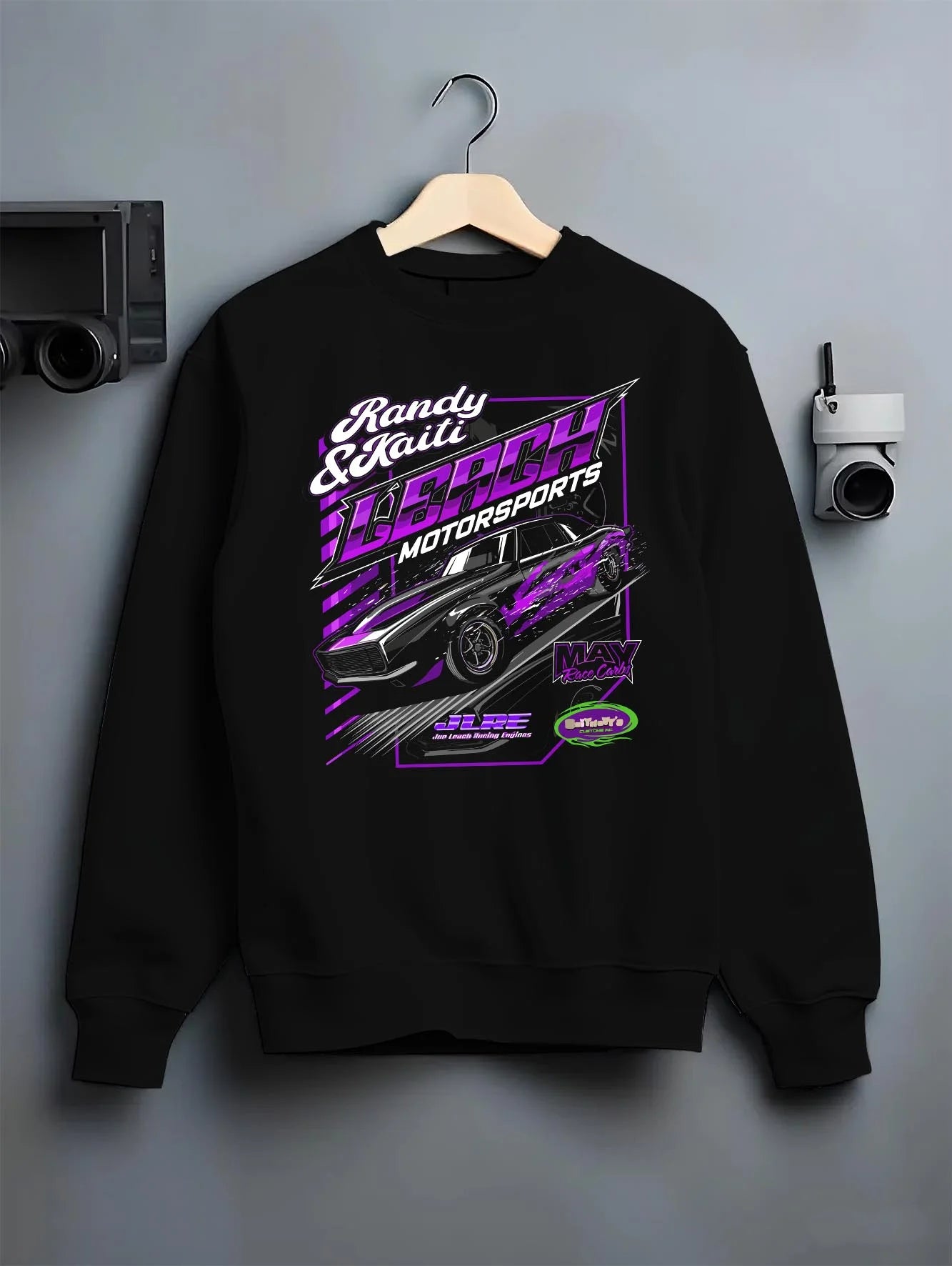 Black crewneck sweatshirt on a hanger against a grey wall, featuring STI street racing performance motorsport automotive randy.