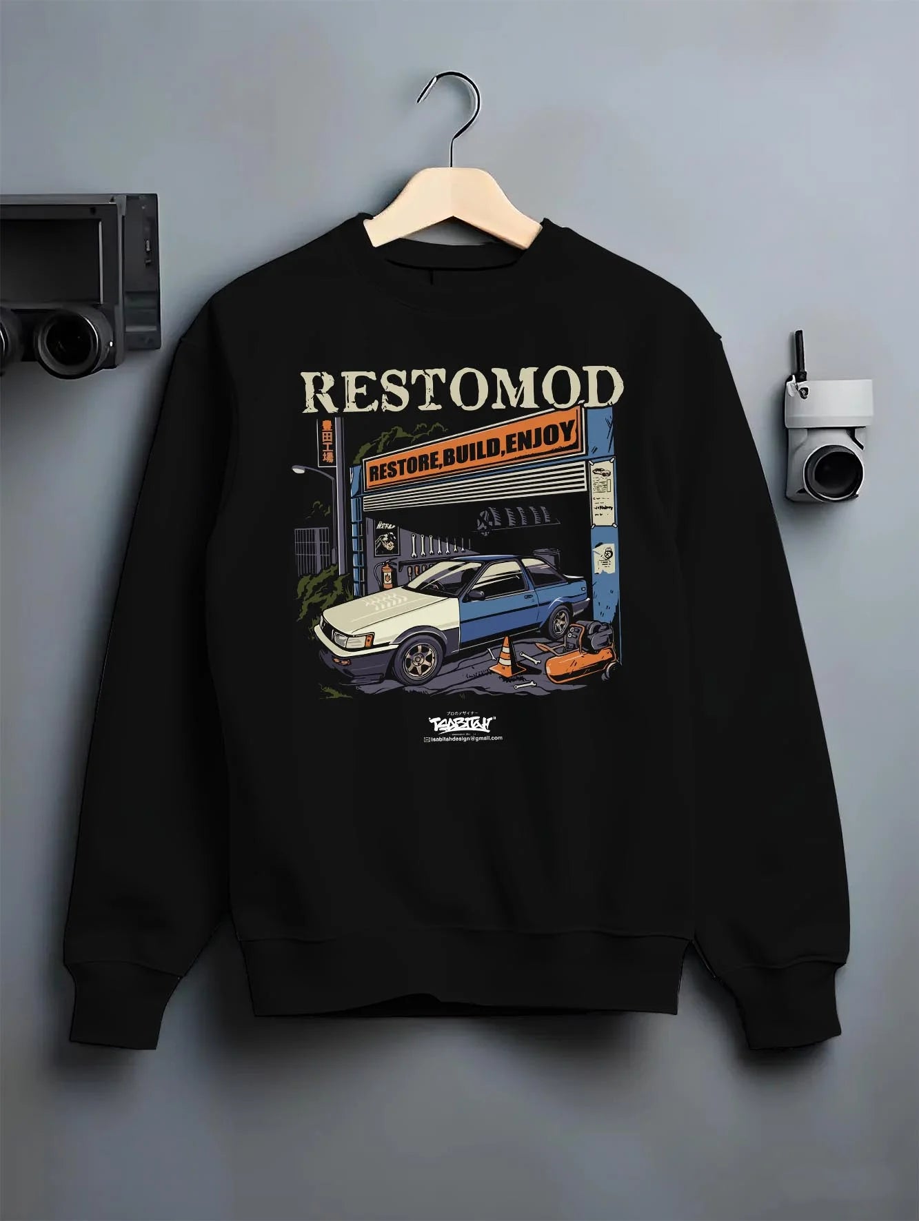Black crewneck sweatshirt on a hanger against a grey wall, featuring Toyota AE86 drift jdm tuner street racing performance graphic.