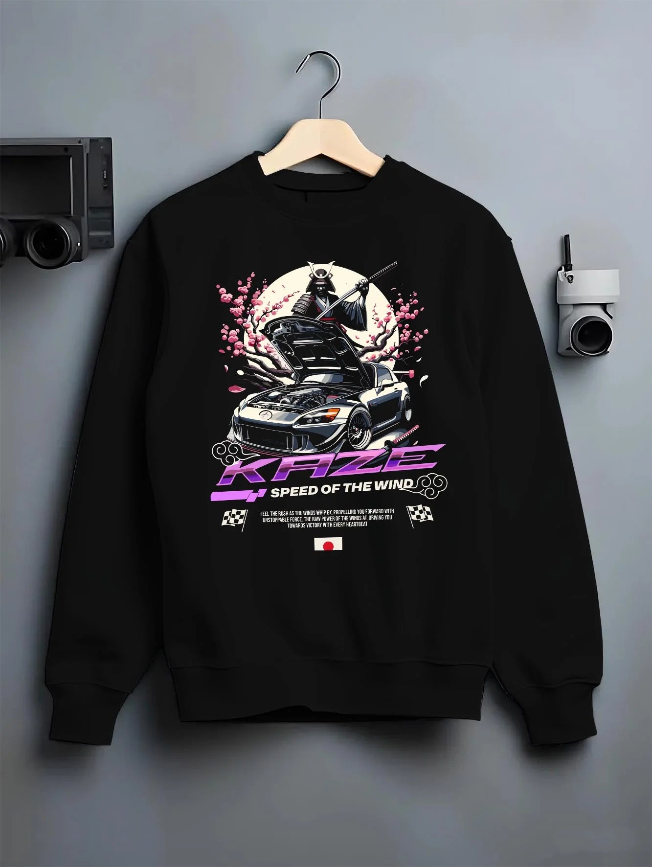 Black crewneck sweatshirt on a hanger against a grey wall, featuring drift japanese street retro racing performance graphic.