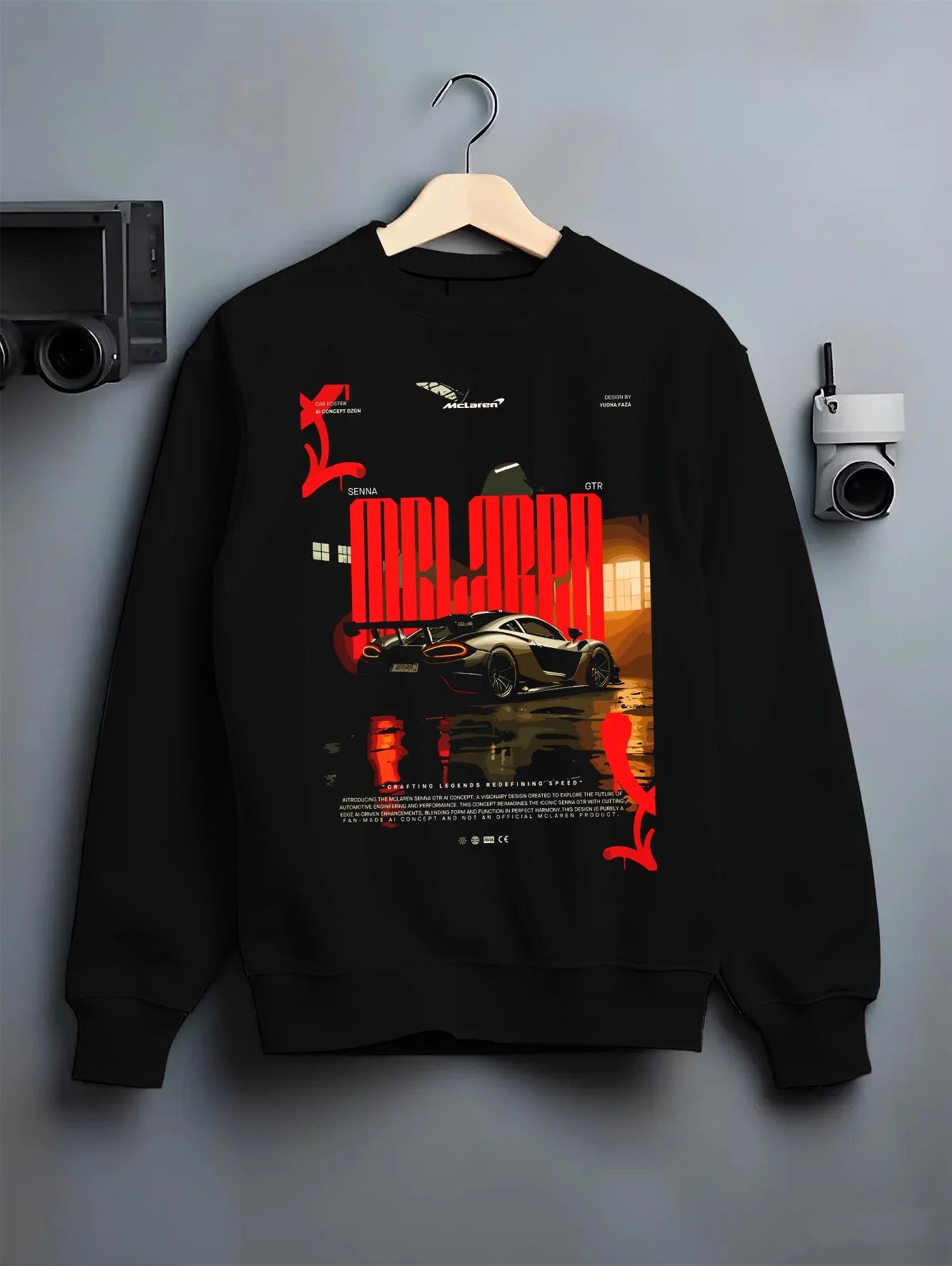 Black crewneck sweatshirt on a hanger against a grey wall, featuring McLaren SENNA track street racing performance graphic.