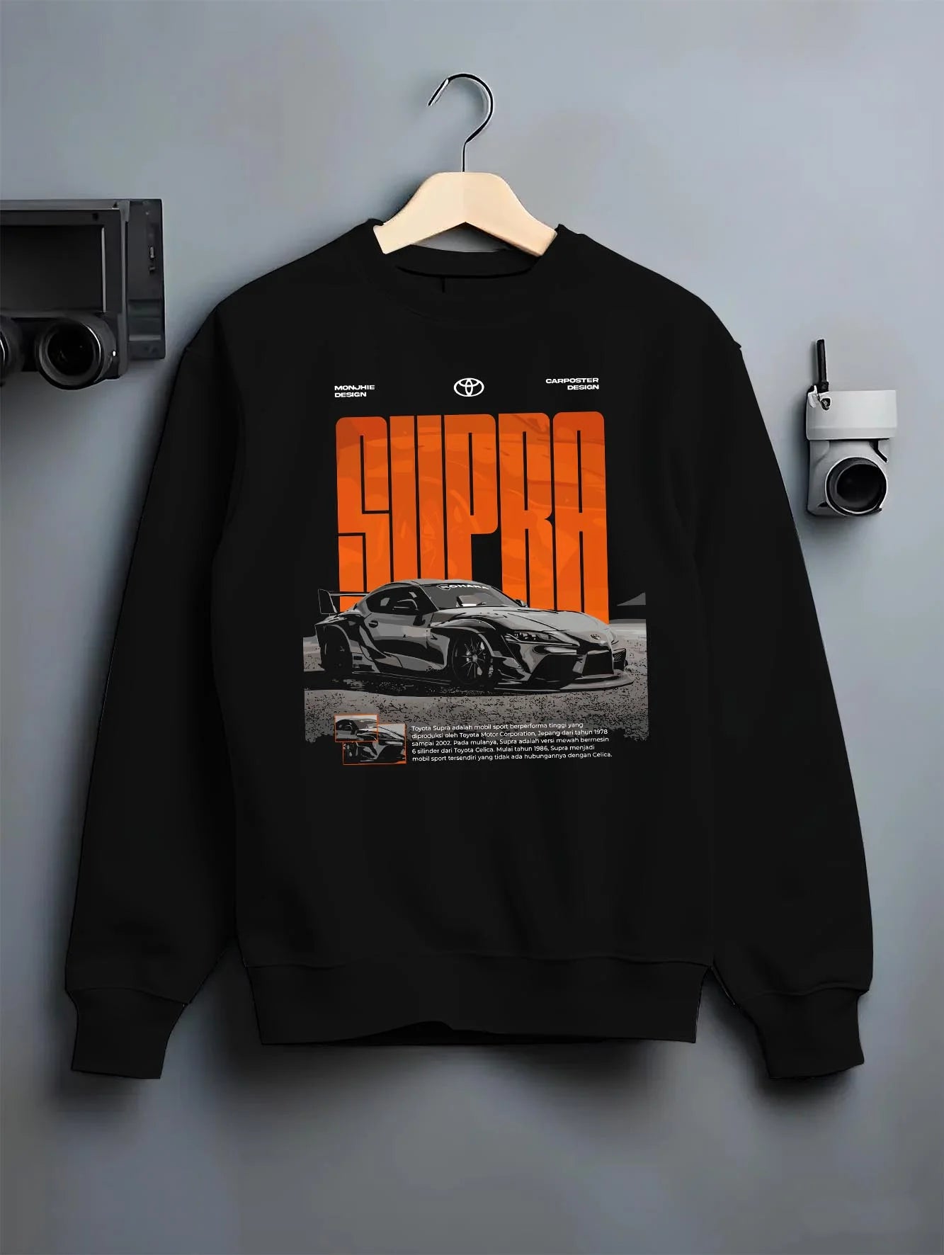 Black crewneck sweatshirt on a hanger against a grey wall, featuring Toyota Supra turbo racing drift jdm japanese tuner supjdm.