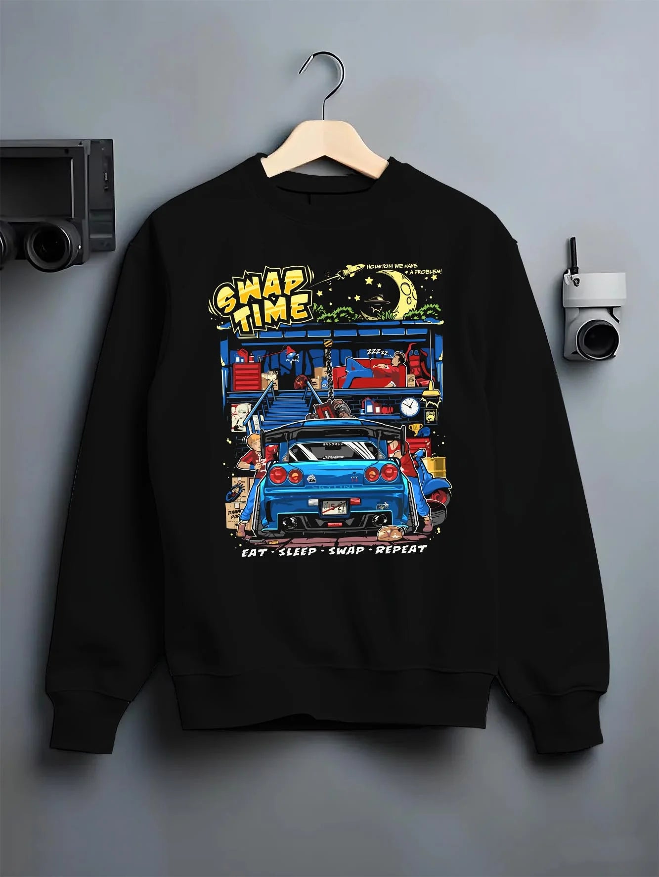 Black crewneck sweatshirt on a hanger against a grey wall, featuring Nissan Skyline R34 r34 skyline racing drift jdm tuner graphic.