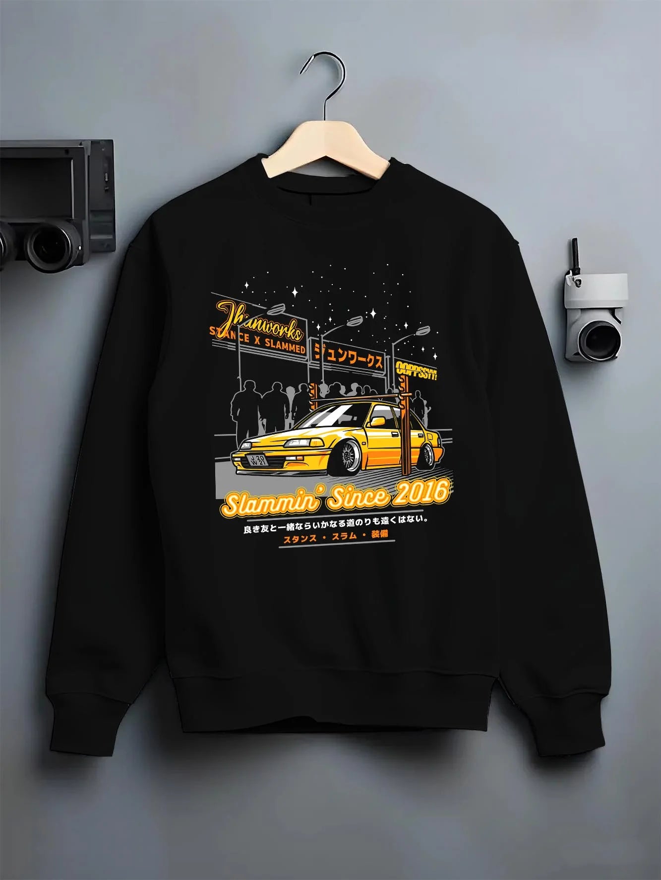 Black crewneck sweatshirt on a hanger against a grey wall, featuring Honda rs type r racing motorsport jdm street graphic.