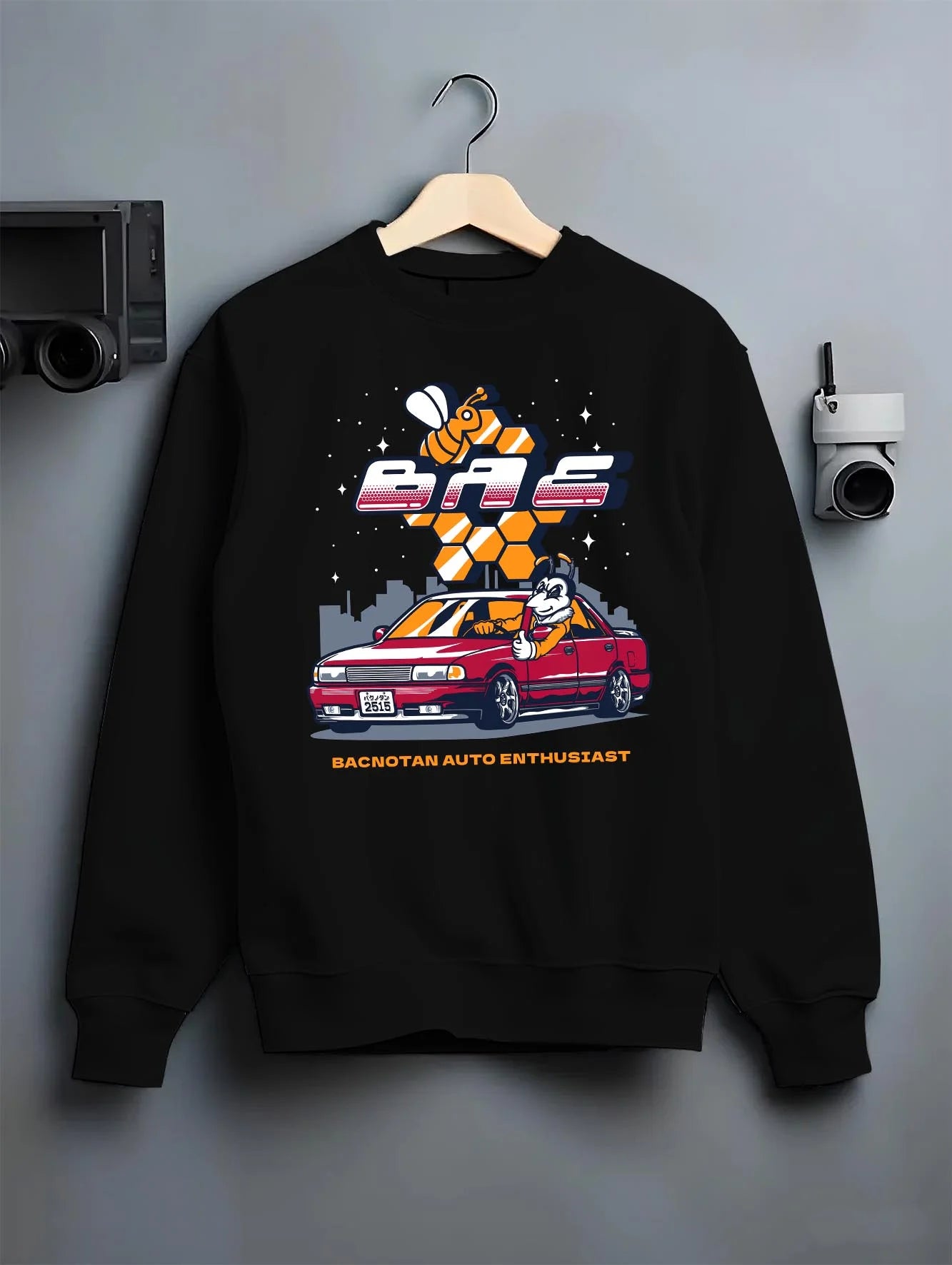 Black crewneck sweatshirt on a hanger against a grey wall, featuring street retro enthusiast racing performance motorsport graphic.