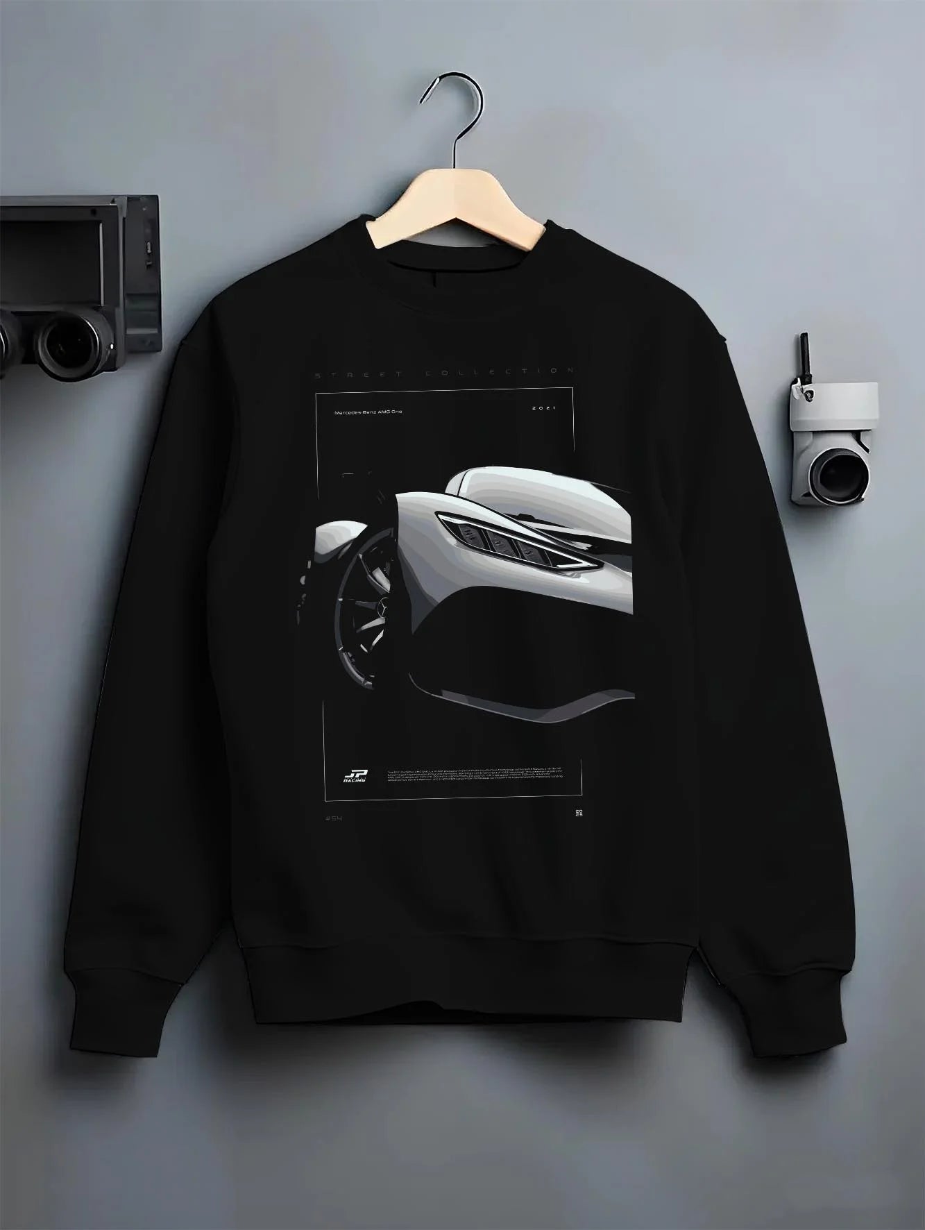 Black crewneck sweatshirt on a hanger against a grey wall, featuring Mercedes-Benz AMG rs racing motorsport street graphic.