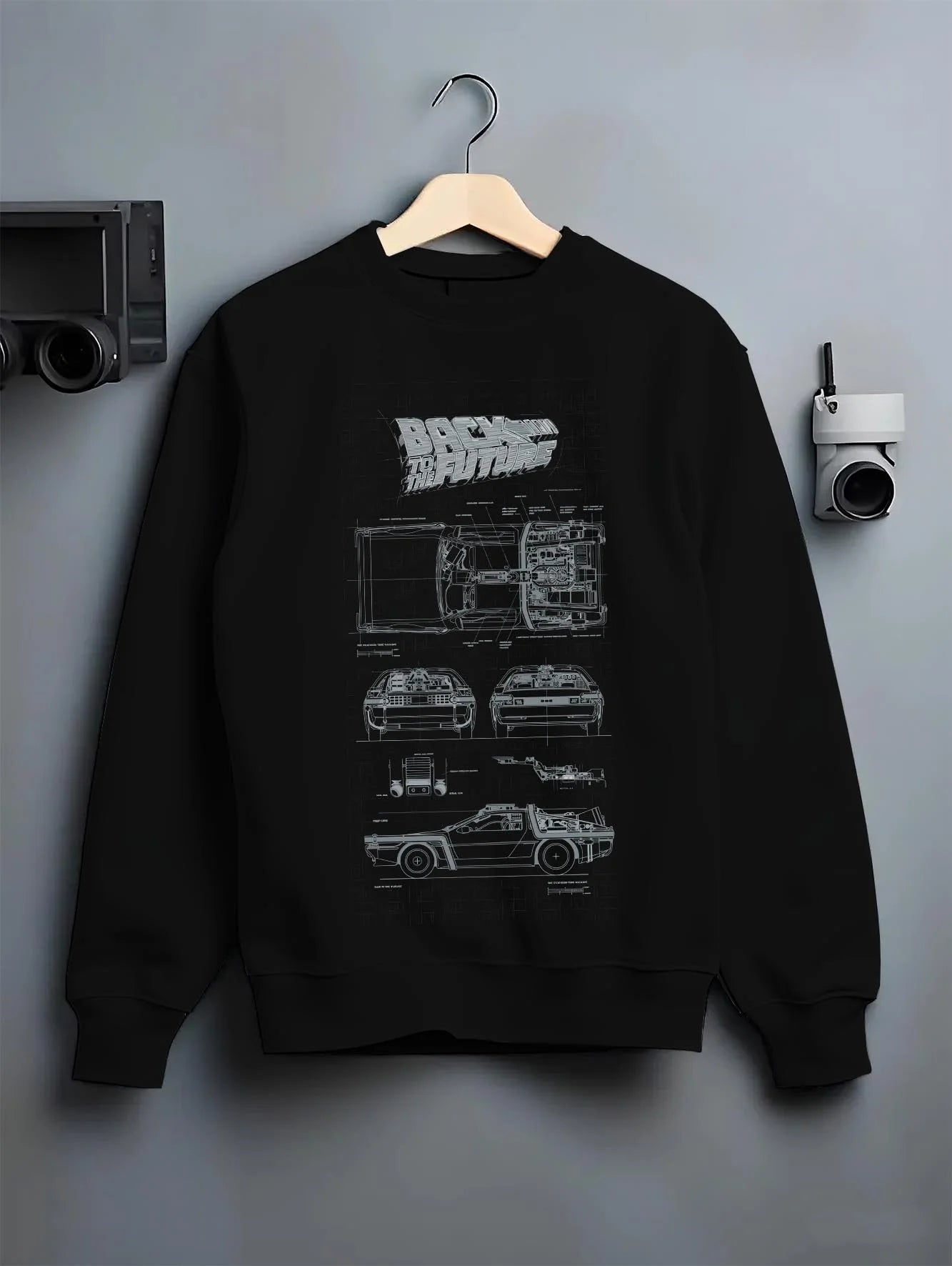 Black crewneck sweatshirt on a hanger against a grey wall, featuring DeLorean DMC-12 street retro racing performance graphic.