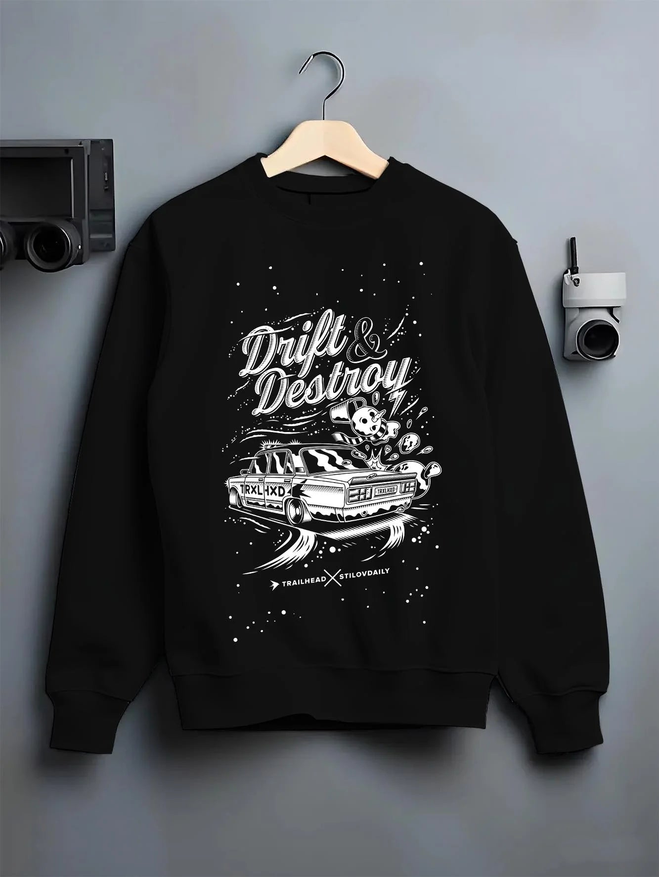 Black crewneck sweatshirt on a hanger against a grey wall, featuring racing drift street retro performance motorsport graphic.