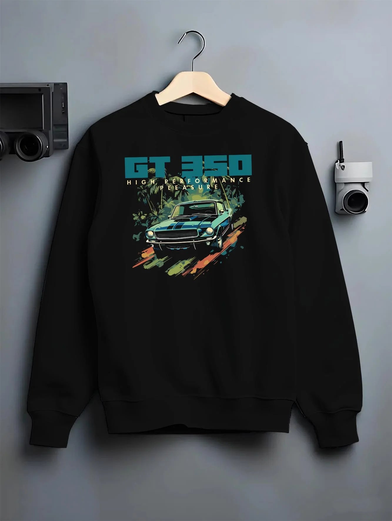 Black crewneck sweatshirt on a hanger against a grey wall, featuring Ford Mustang street retro classic enthusiast racing graphic.
