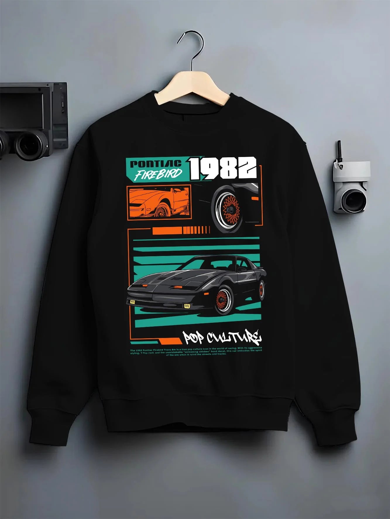 Black crewneck sweatshirt on a hanger against a grey wall, featuring Pontiac firebird trans am racing muscle street retro graphic.