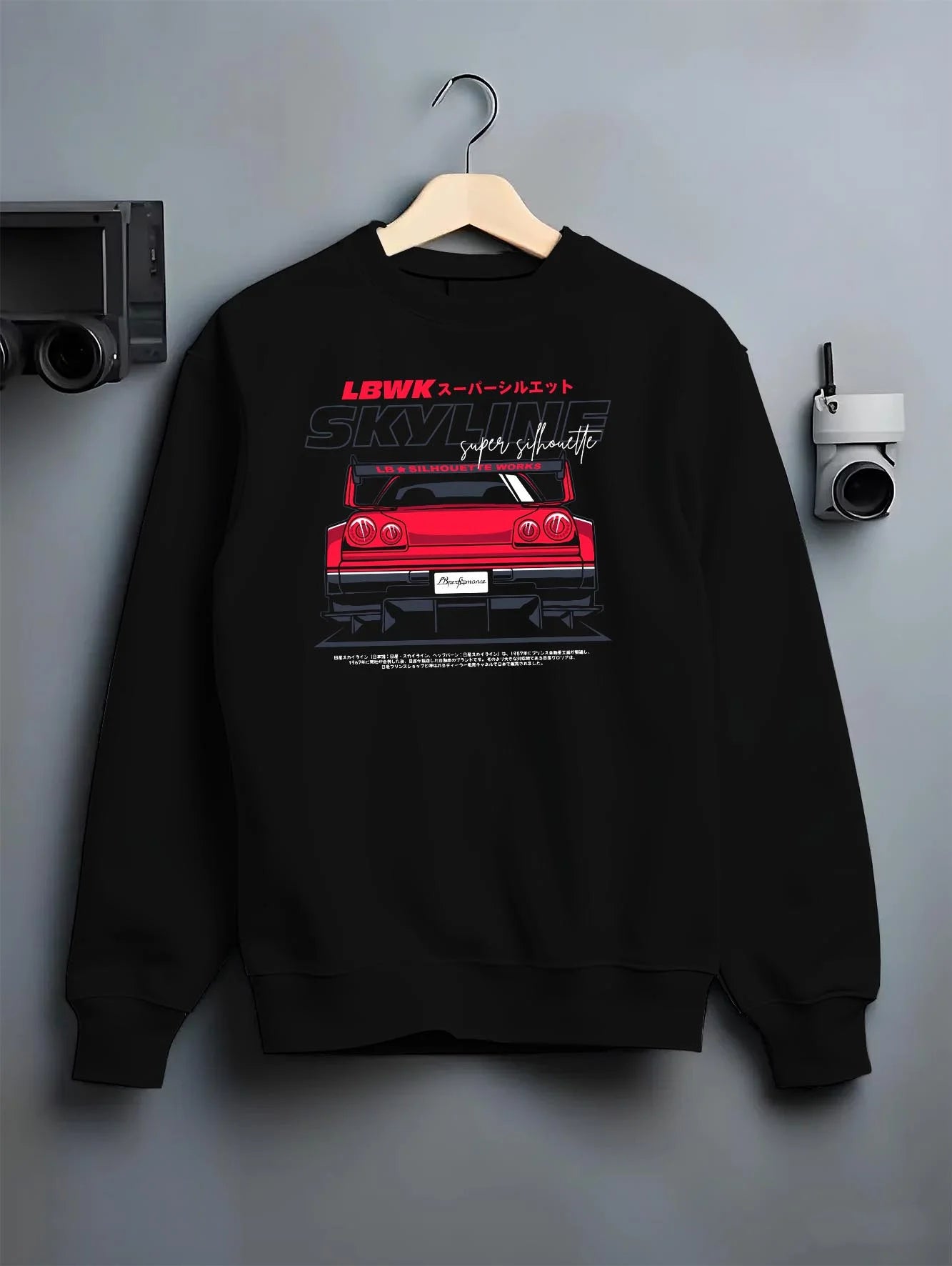 Black crewneck sweatshirt on a hanger against a grey wall, featuring NISSAN SKYLINE racing jdm widebody liberty walk street graphic.