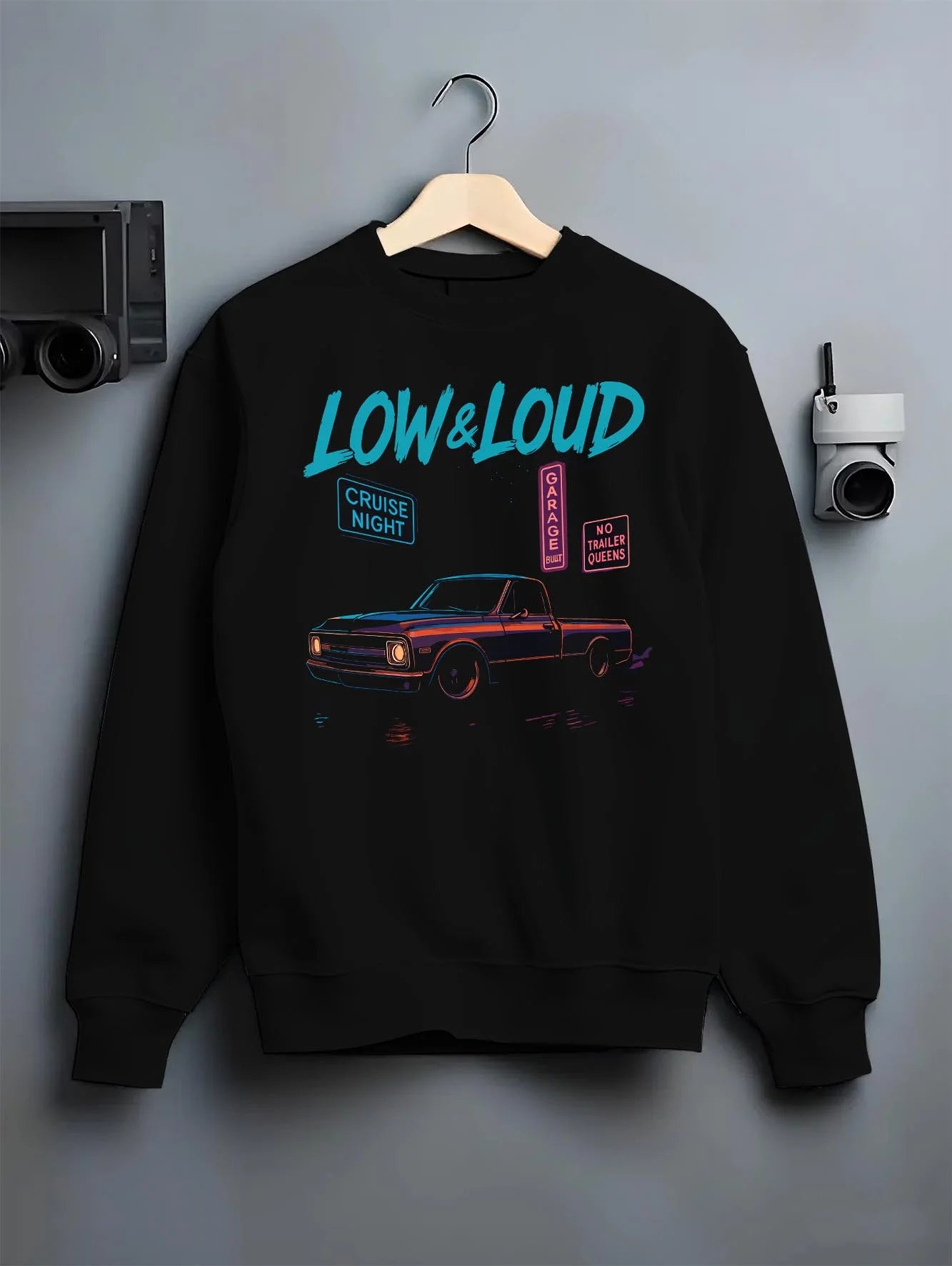 Black crewneck sweatshirt on a hanger against a grey wall, featuring street retro classic racing performance motorsport graphic.
