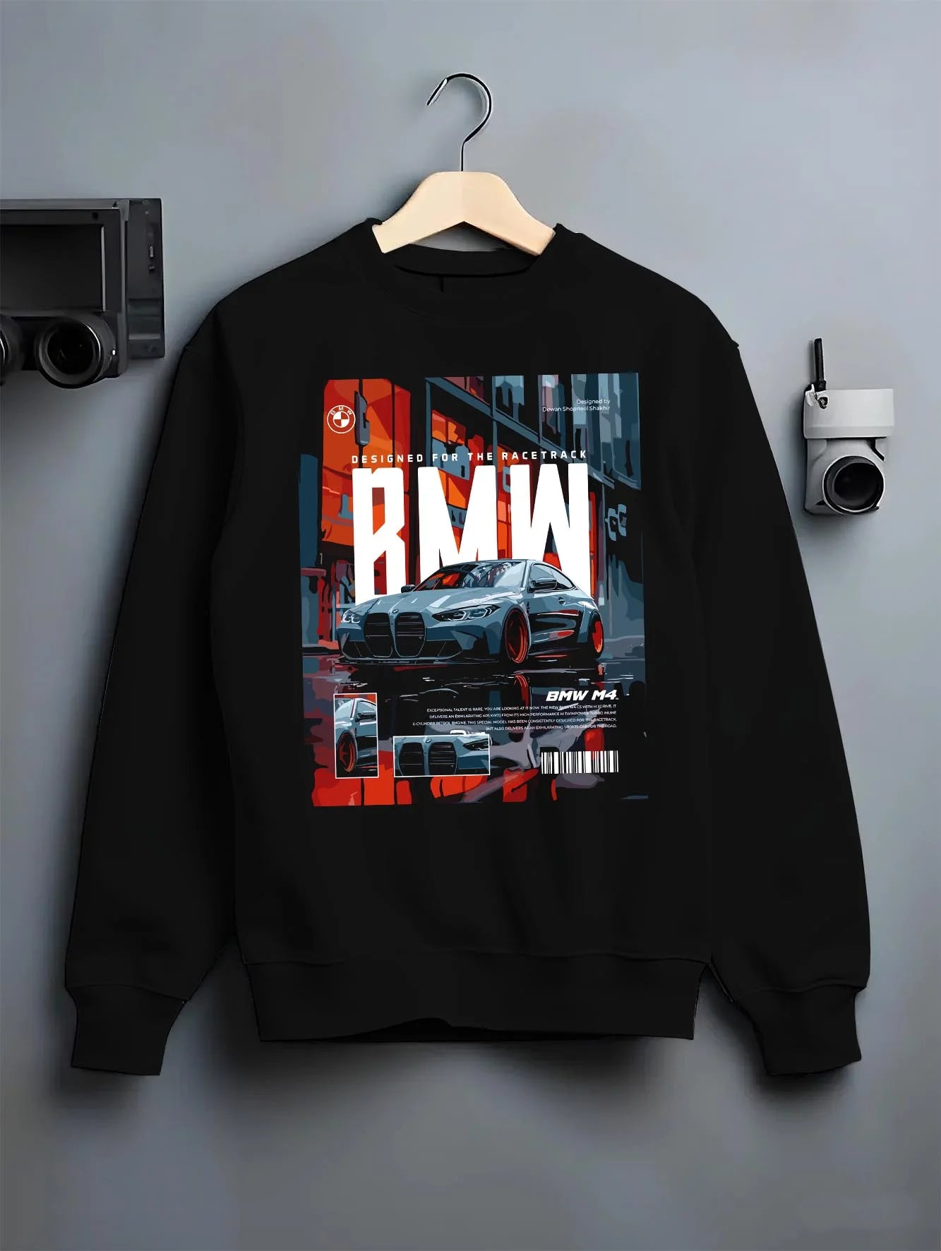 Black crewneck sweatshirt on a hanger against a grey wall, featuring BMW M4 rs turbo racing motorsport track german street graphic.