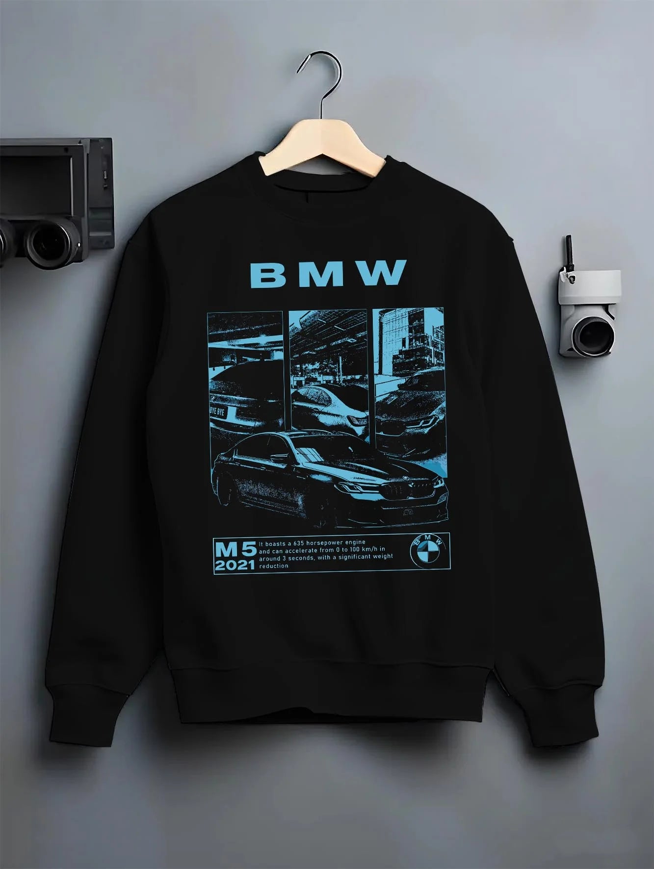 Black crewneck sweatshirt on a hanger against a grey wall, featuring BMW M5 rs turbo racing motorsport euro german street graphic.