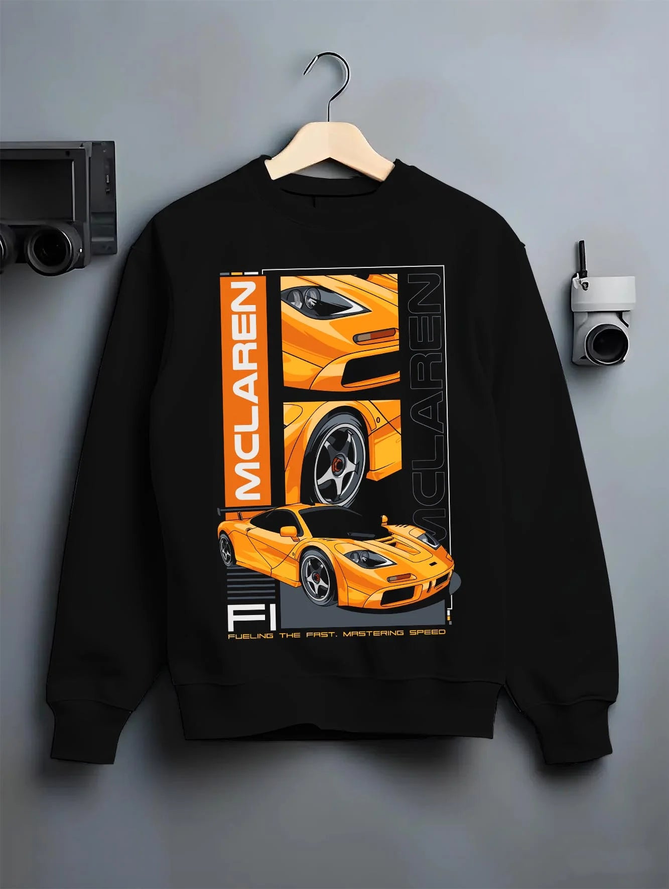 Black crewneck sweatshirt on a hanger against a grey wall, featuring McLaren 720S rs racing enthusiast street performance graphic.