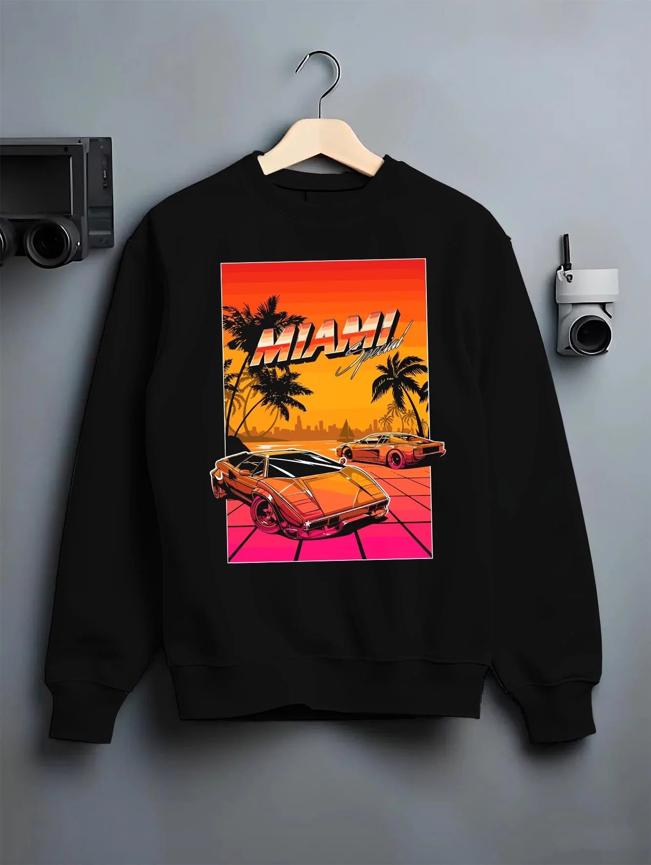 Black crewneck sweatshirt on a hanger against a grey wall, featuring street retro racing performance motorsport automotive miams1.