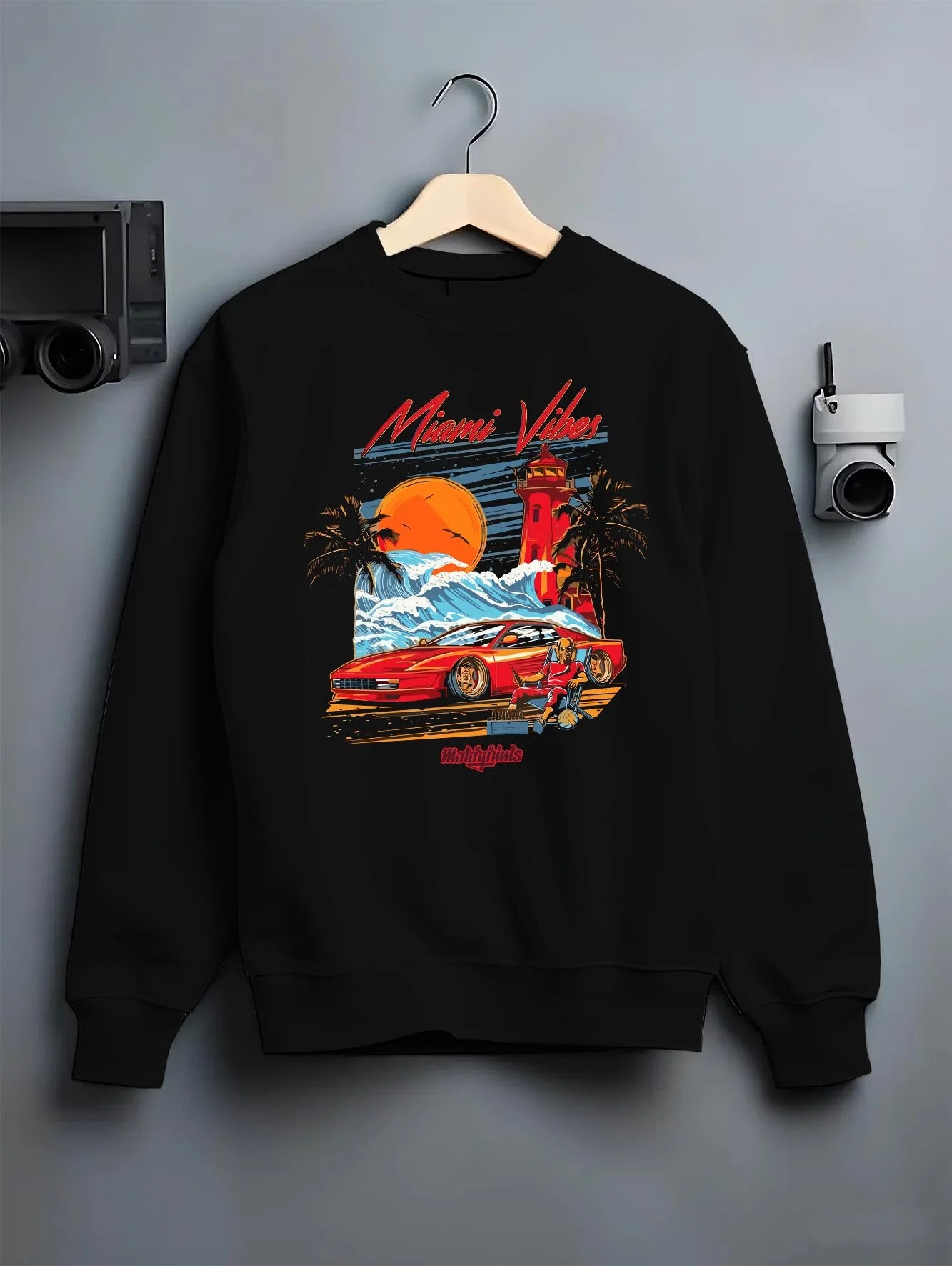 Black crewneck sweatshirt on a hanger against a grey wall, featuring street retro racing performance motorsport automotive miamv1.