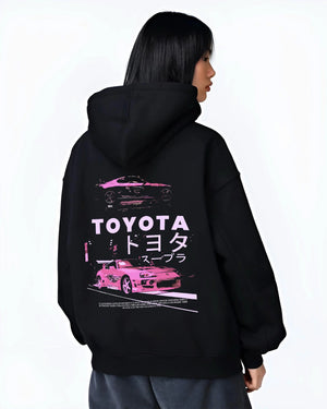 Black hoodie worn by a female model, back view, featuring Toyota Supra racing drift jdm japanese tuner street retro graphic.