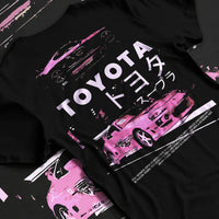 Black T-shirt laid flat with natural fabric folds, featuring Toyota Supra racing drift jdm japanese tuner street retro graphic.