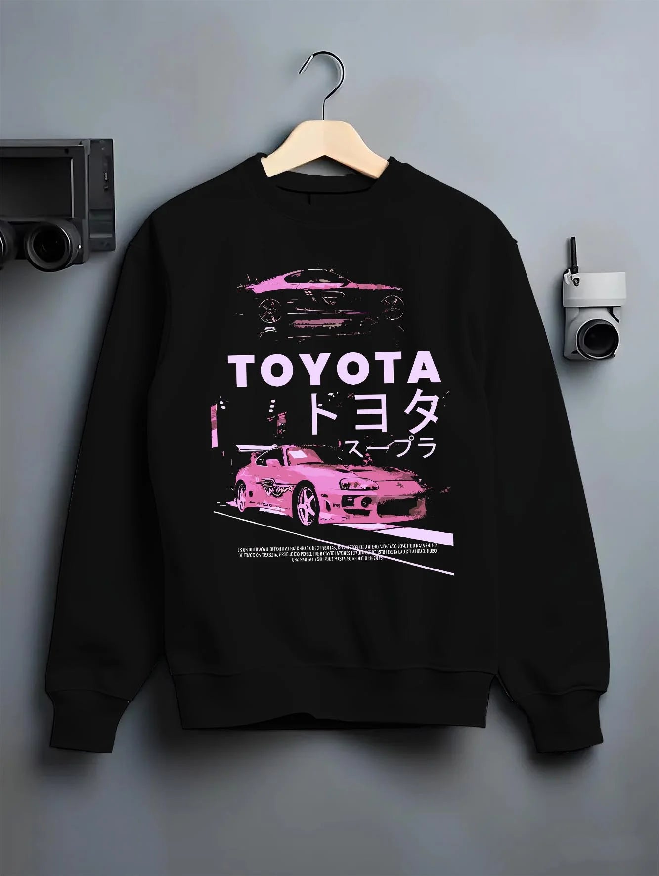 Black crewneck sweatshirt on a hanger against a grey wall, featuring Toyota Supra racing drift jdm japanese tuner street graphic.