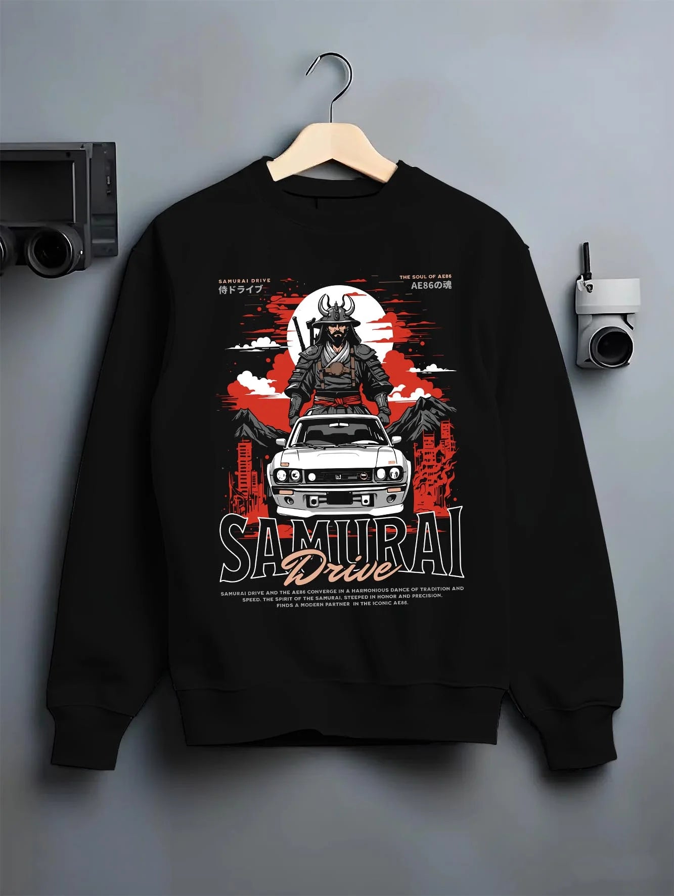 Black crewneck sweatshirt on a hanger against a grey wall, featuring drift japanese street racing performance motorsport graphic.