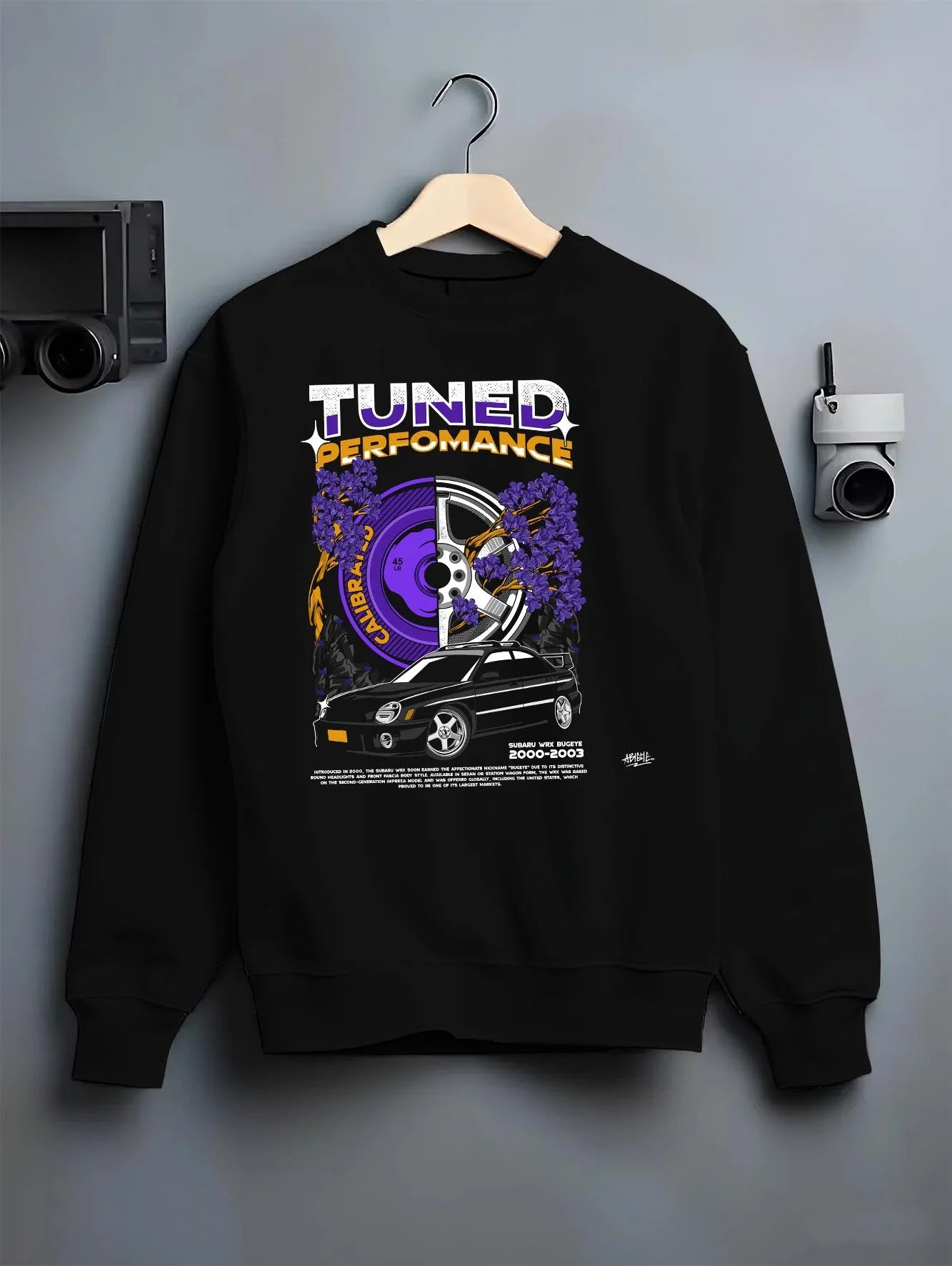 Black crewneck sweatshirt on a hanger against a grey wall, featuring Subaru WRX rally legend racing street performance graphic.