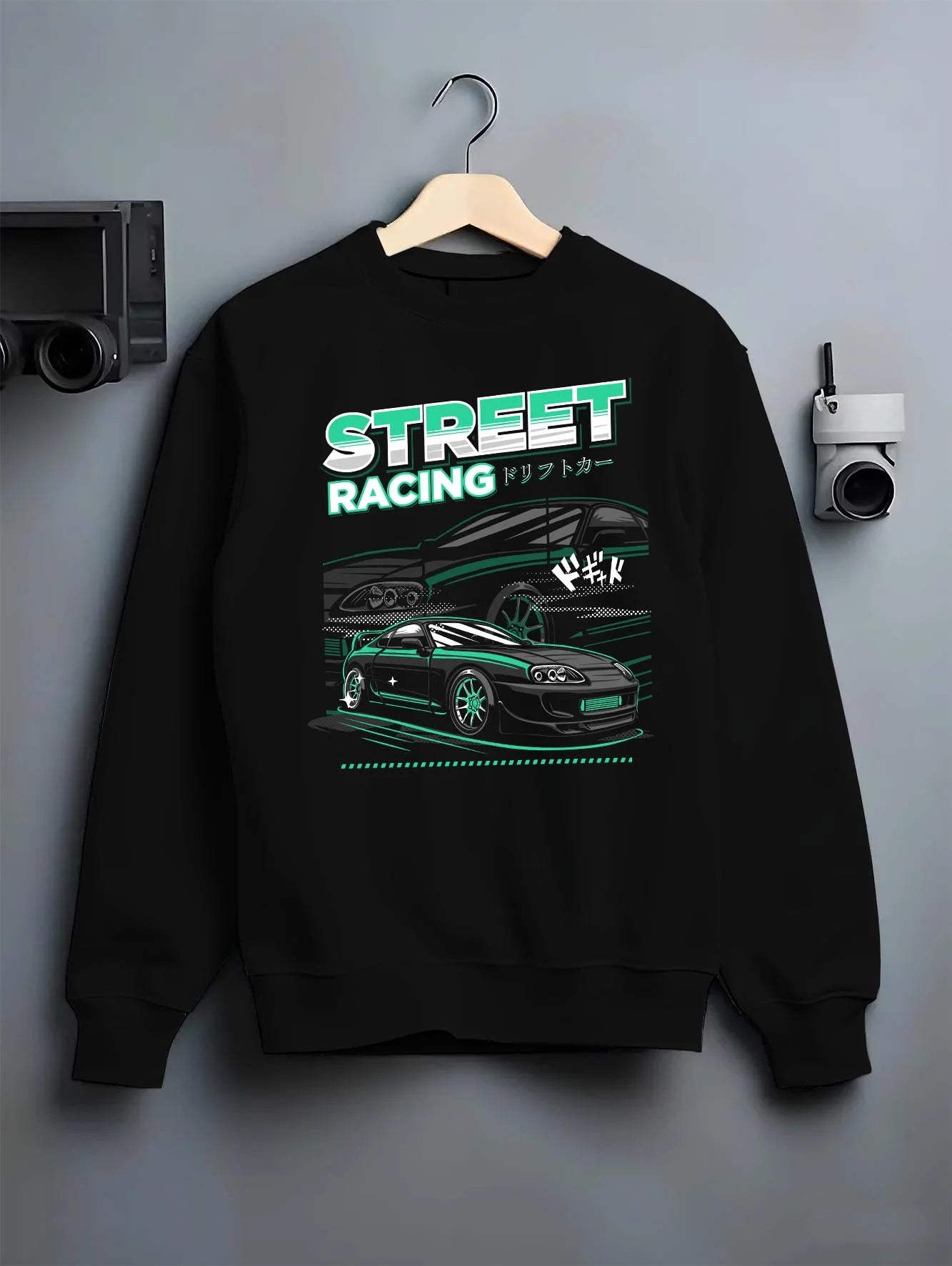 Black crewneck sweatshirt on a hanger against a grey wall, featuring Toyota Supra turbo jdm street racing performance graphic.